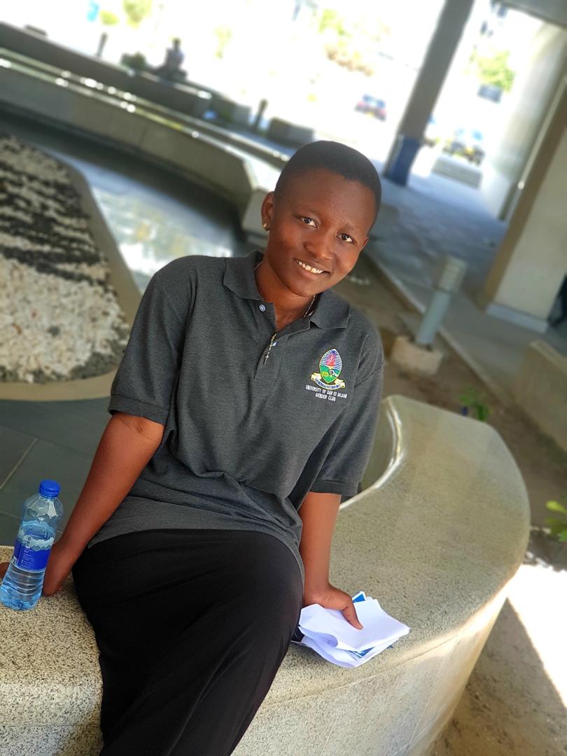 A smiling professional sitting comfortably on the lush green campus grounds of the University of Dar es Salaam.