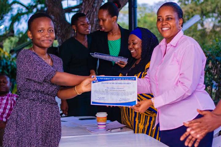 A formal photograph of a student leader proudly receiving an official leadership certificate from Dr. Lulu Mahai at the University of Dar es Salaam.
