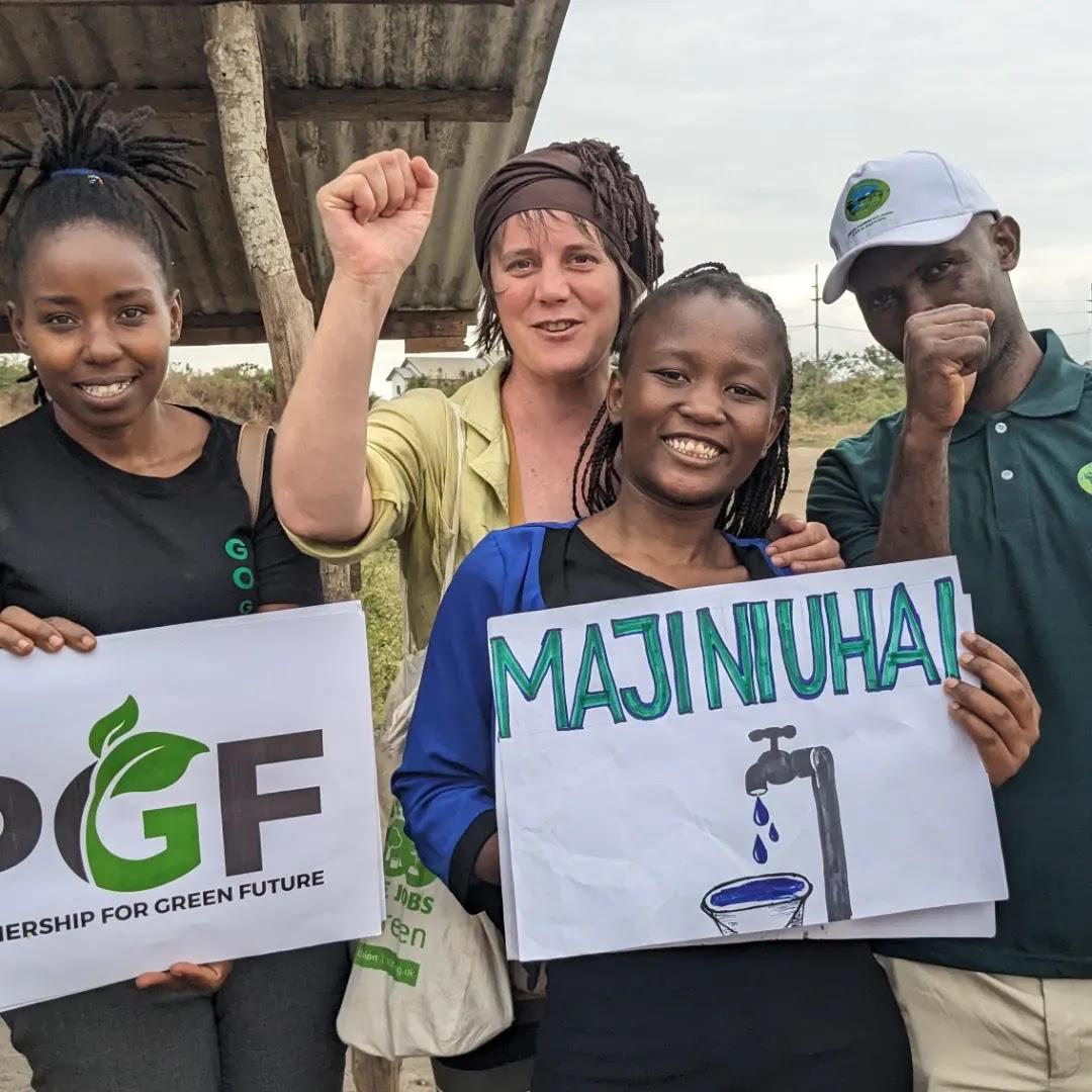 An environmental advocate standing with community members holding a banner that reads "Maji ni Uhai" during a safe water campaign for schools.