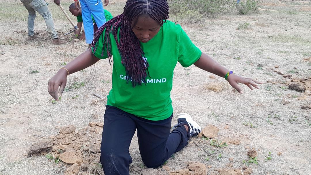 An environmental founder planting a tree seedling alongside enthusiastic students at a school in the Manyara Region during a Green Mind Project campaign.