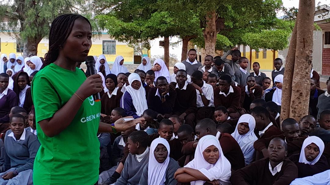 A mentor leaning in and talking warmly with a group of secondary school students inside a classroom.