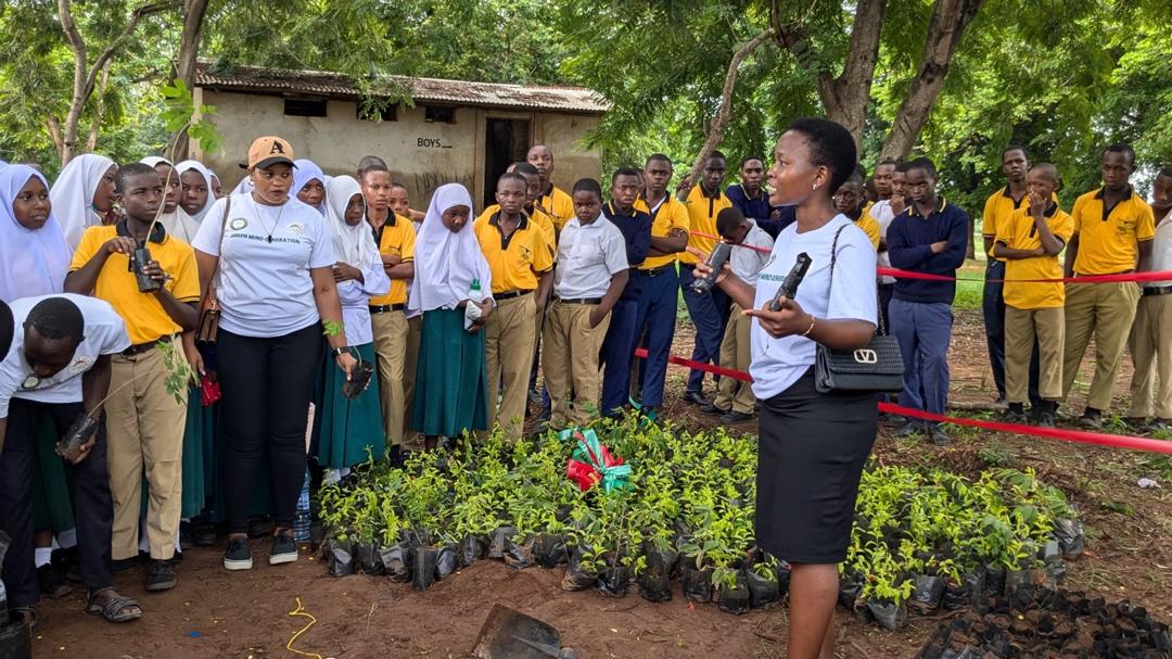 An environmental educator demonstrating soil preparation and seedling care to a group of attentive students around a newly built school tree nursery bed in Kilwa.